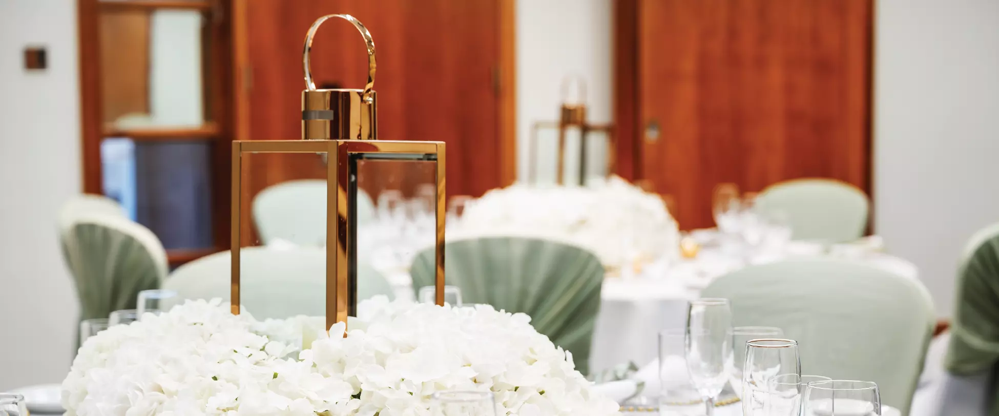 Tables set up for a wedding breakfast with white table covers, white floral bouquets and gold lanterns..