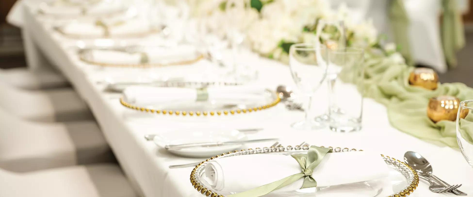 A table set up for the wedding party for a wedding breakfast. The table has a green and gold decorations..